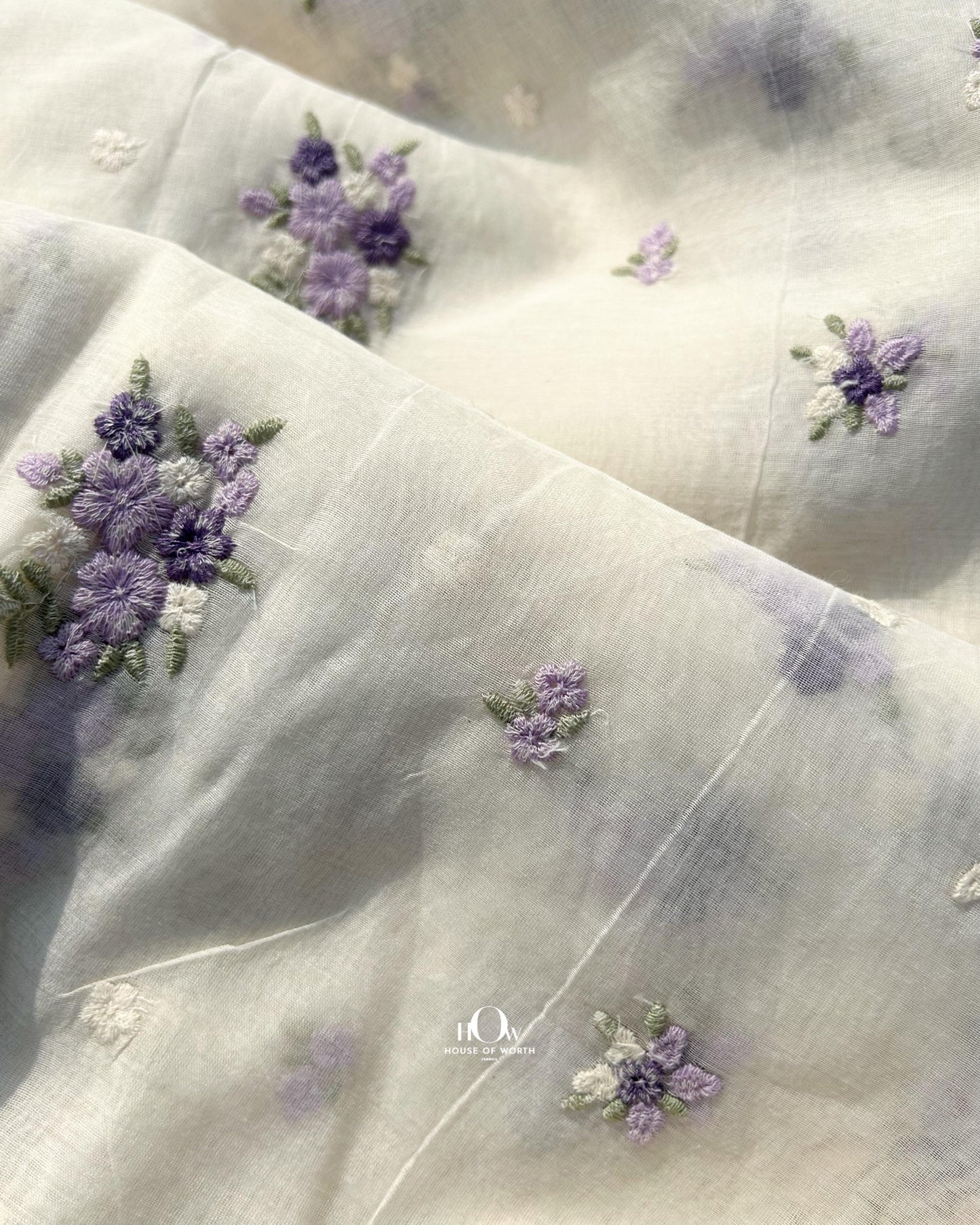 Off-white handwoven Mul Chanderi fabric with pastel floral embroidery – dyeable fabric for boutique and festive wear.