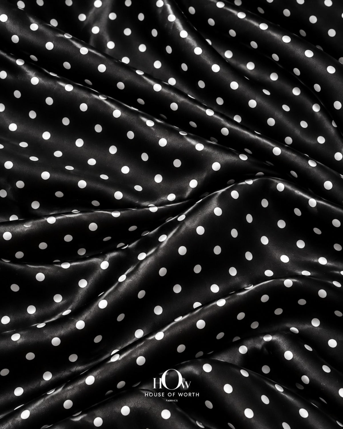Draped black polka dot satin showing graceful folds and a repeating white dot pattern