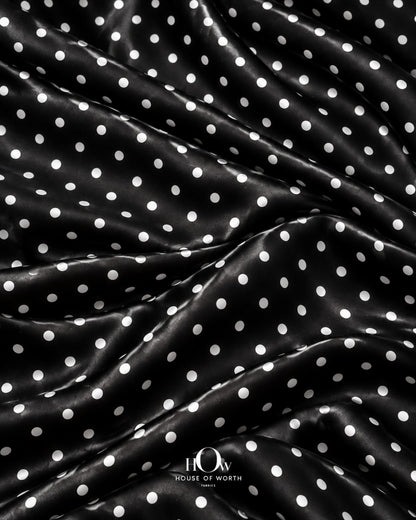 Draped black polka dot satin showing graceful folds and a repeating white dot pattern