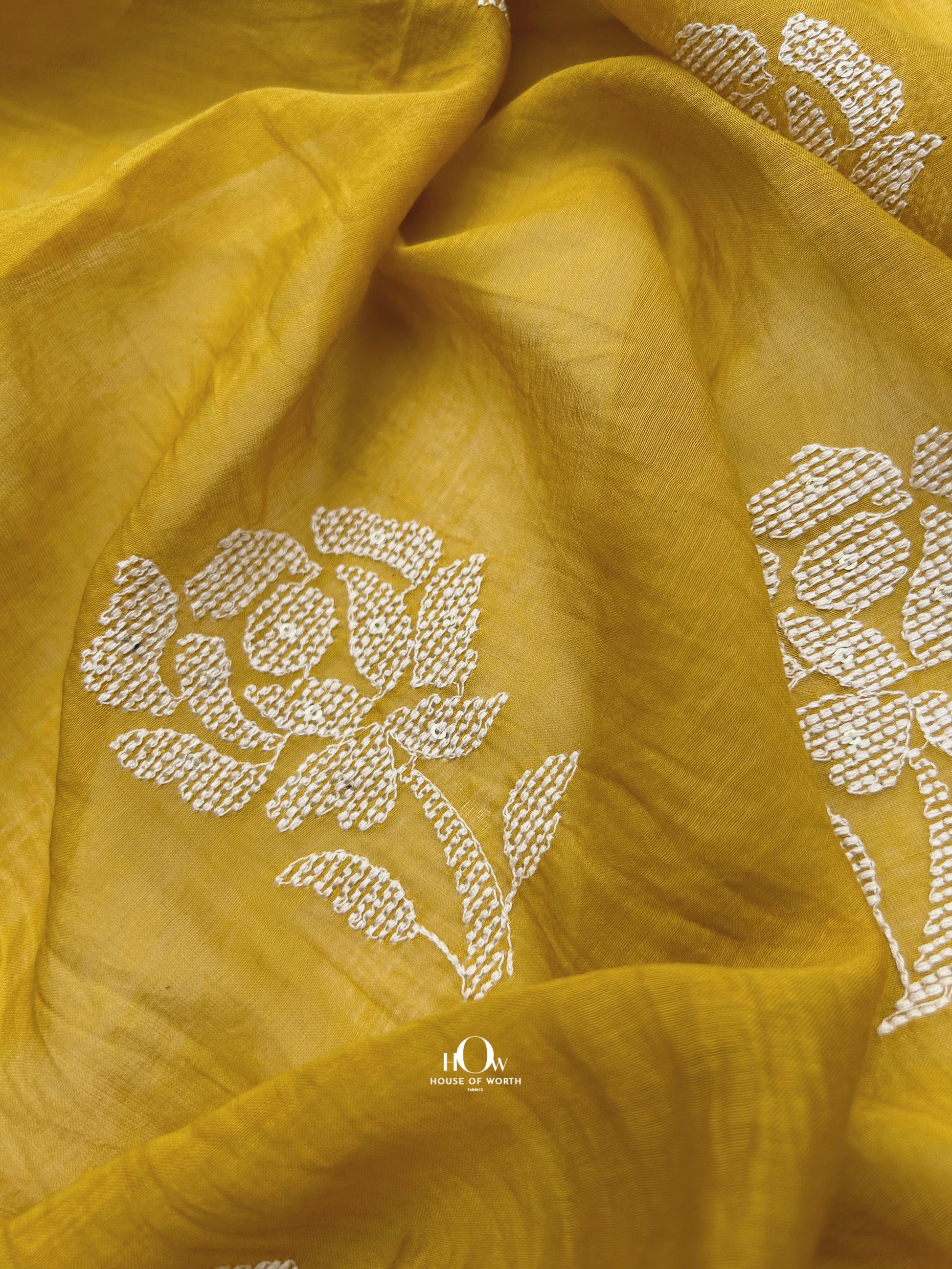 Bright yellow Mul Chanderi fabric with white floral embroidery – perfect for festive sarees, suits, and ethnic wear.