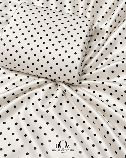 White polka dot satin fabric with evenly spaced black dots and a smooth satin sheen